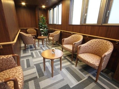 窓からの光が優しく入る部屋。壁には手すりが設置され、高級感のある一人がけのソファーがいくつかあり小さなテーブルもある。