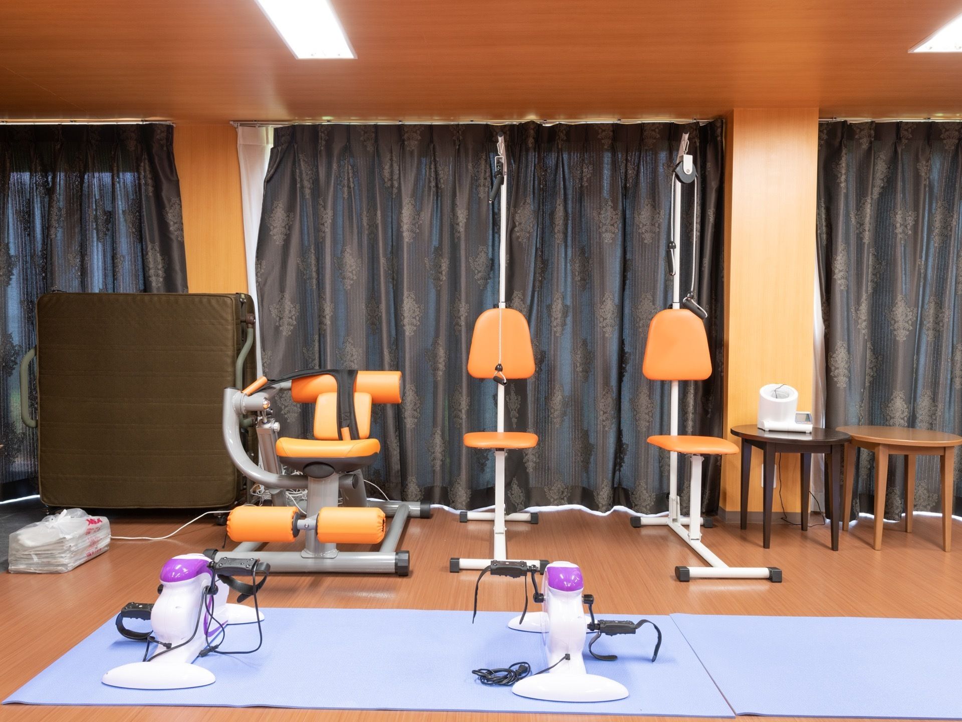 室内運動用の機器が並んでいる。運動前後の体調管理のため、血圧計が置かれている。窓にはカーテンがかけられている。