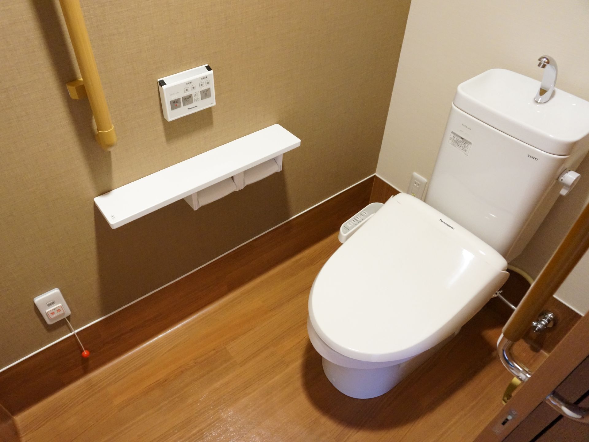 落ち着いた雰囲気のトイレです。壁にボタンがあるウォシュレット付きで、手すりもあるので、立ったり座ったりするときも便利です。