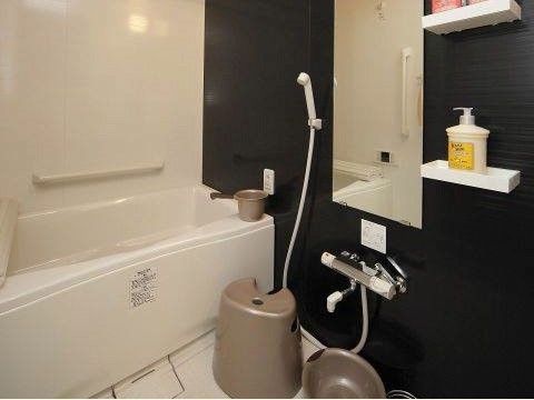白と黒のコントラストがモダンなシステムバス。浴槽横には手すりが設置されている。混合栓のシャワーやカラン、鏡やシャンプーなどが置ける台もある。