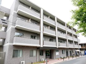 落ち着いた色調の外観で、4階建ての建物です。ガーデンチェアとテーブルがエントランス近くに設置されていて会話を楽しめる。