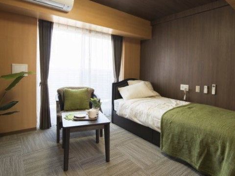 ベッドやテーブルセットが配置された白とグリーンを基調とした居室