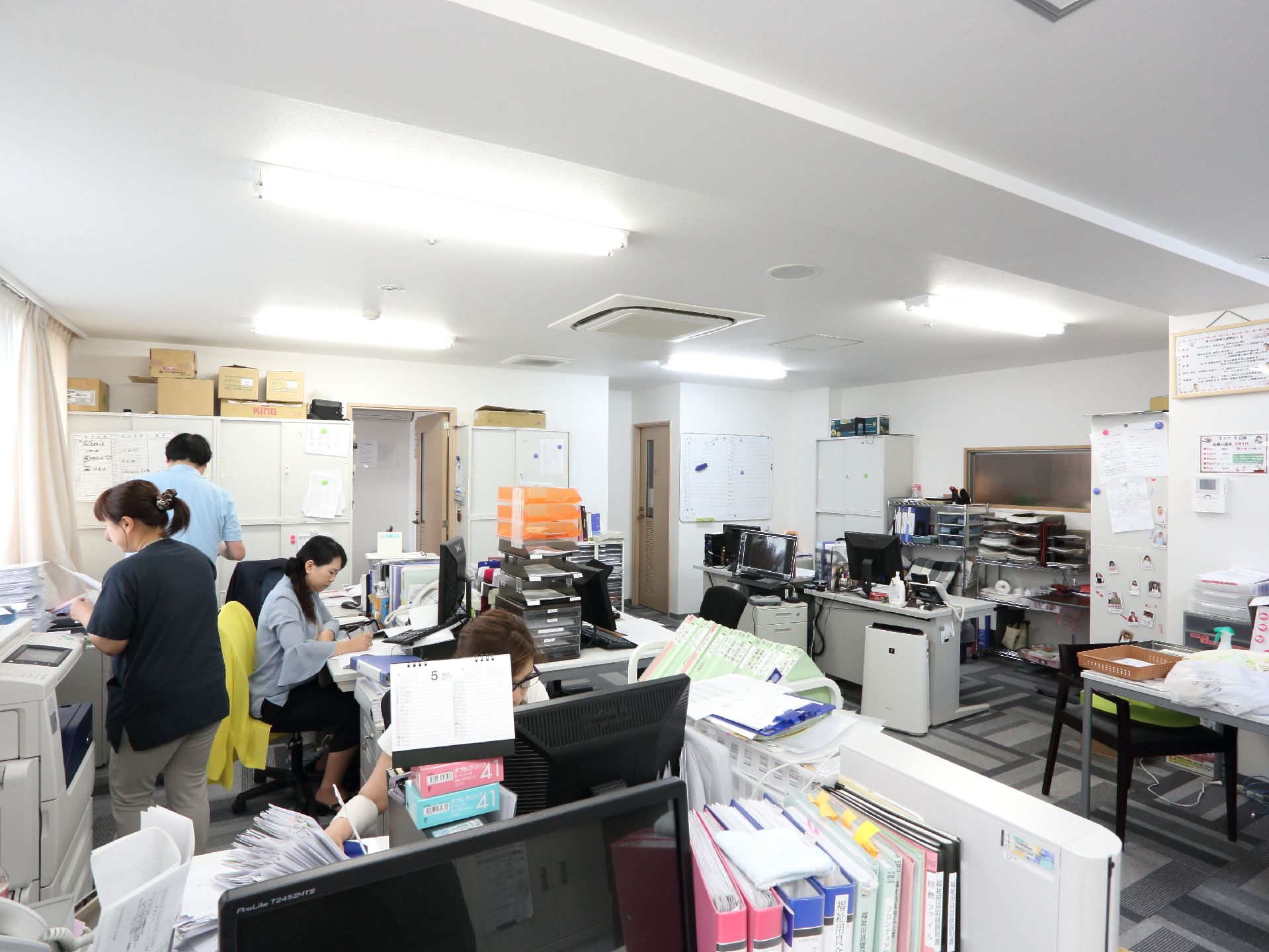 明るく白を基調としたスタッフルームではたくさんの書類が管理されています。パソコンも各デスクにあり、スタッフが作業を行っています。