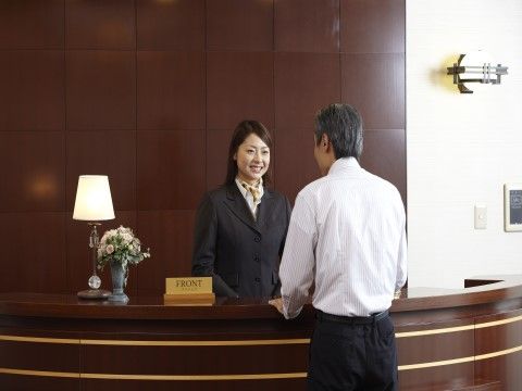 ダークブラウンの受付カウンターで白いシャツの男性の応対をしている女性職員