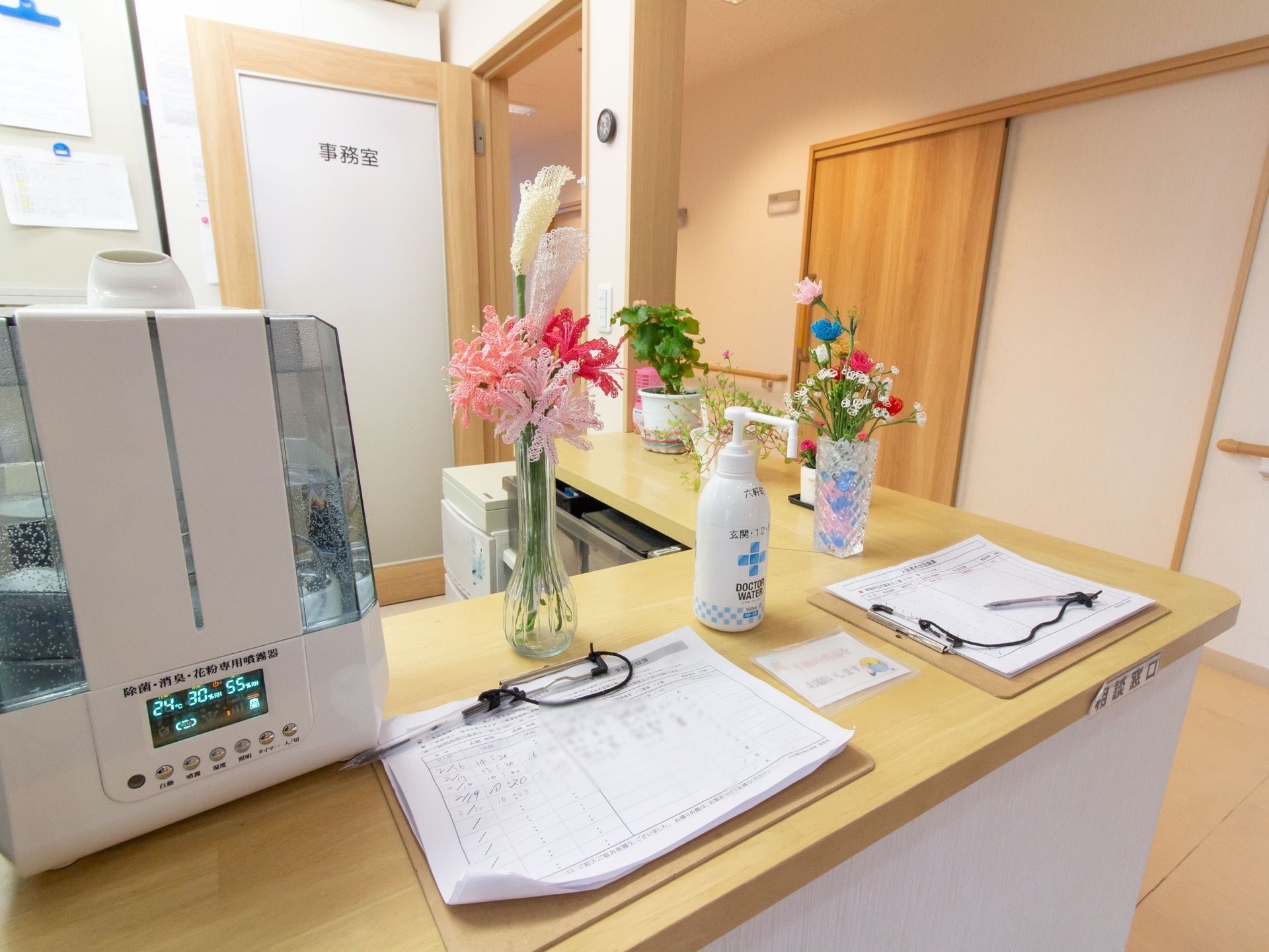 居室の前に事務室が設けられている。カウンターの上には加湿器や受付表が置かれており、花が飾られている。