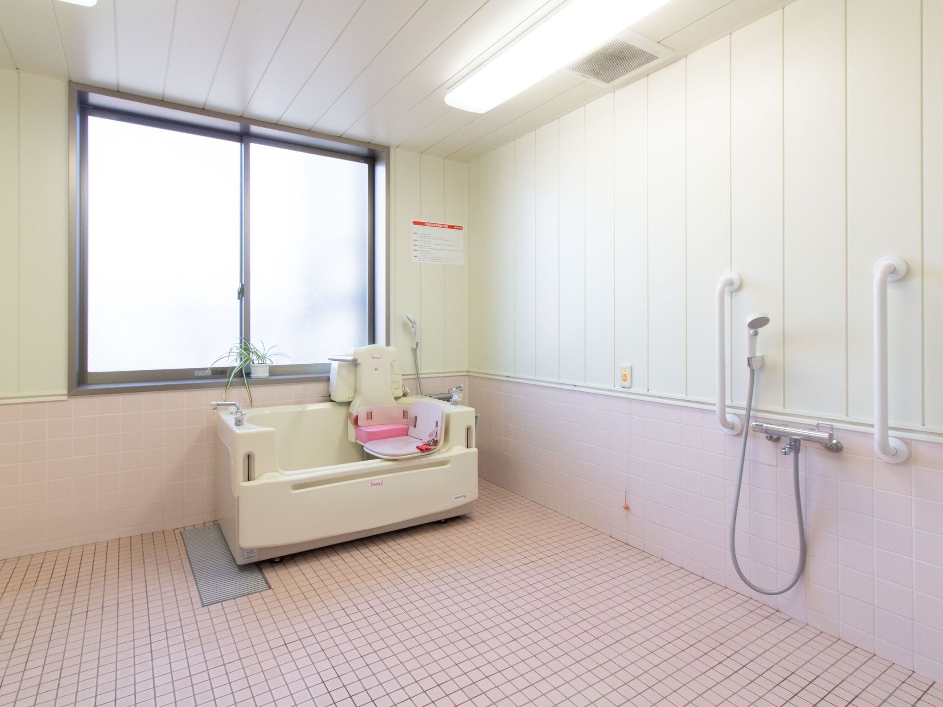 白を基調とした広々とした機械浴室である。大きな窓から外光が差し込んでいる。壁にはナースコールが設置されている。