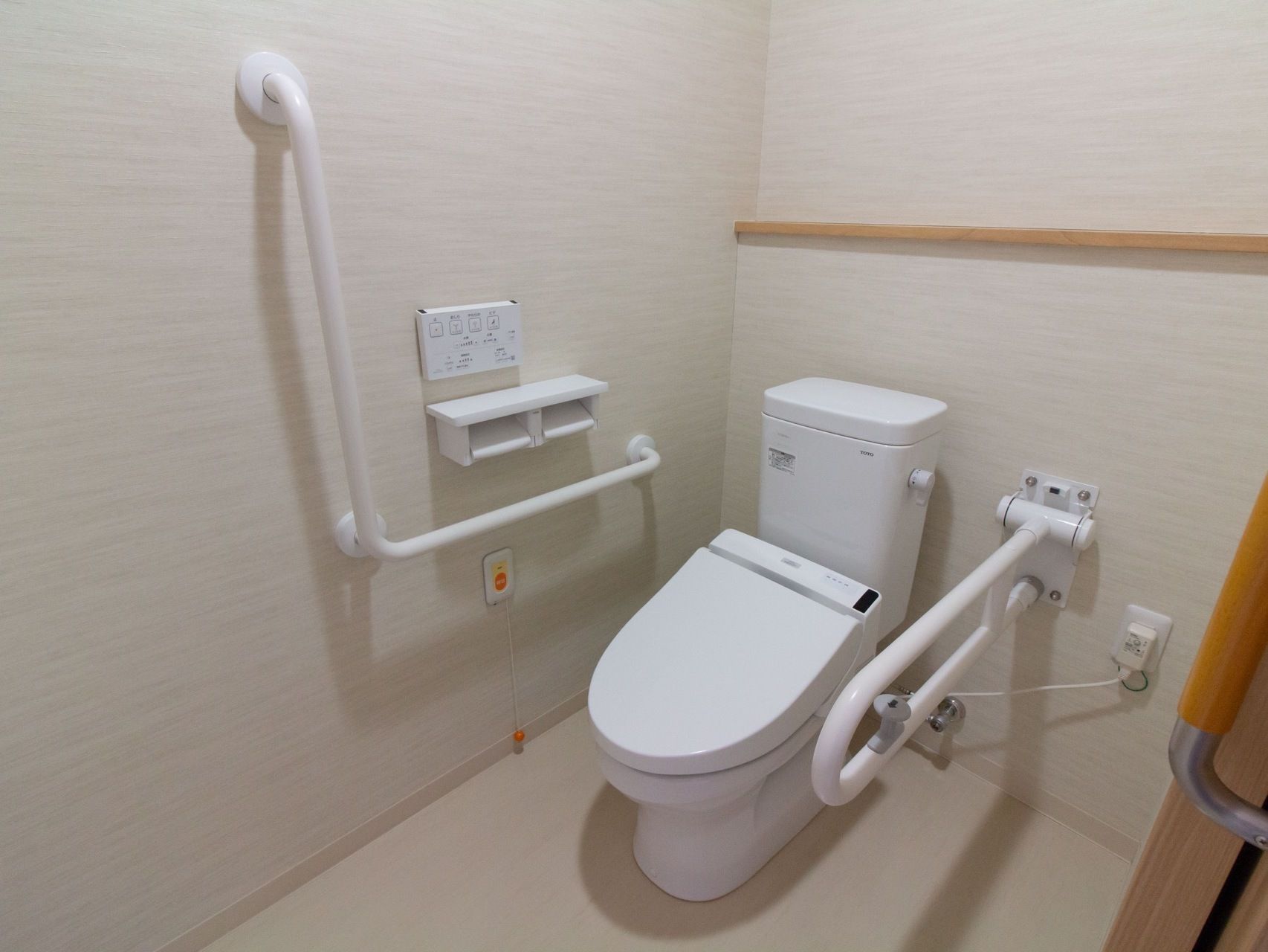 温水洗浄機能付きのトイレが設置されている。壁にはナースコールや手すり、操作パネルが取りつけられている。