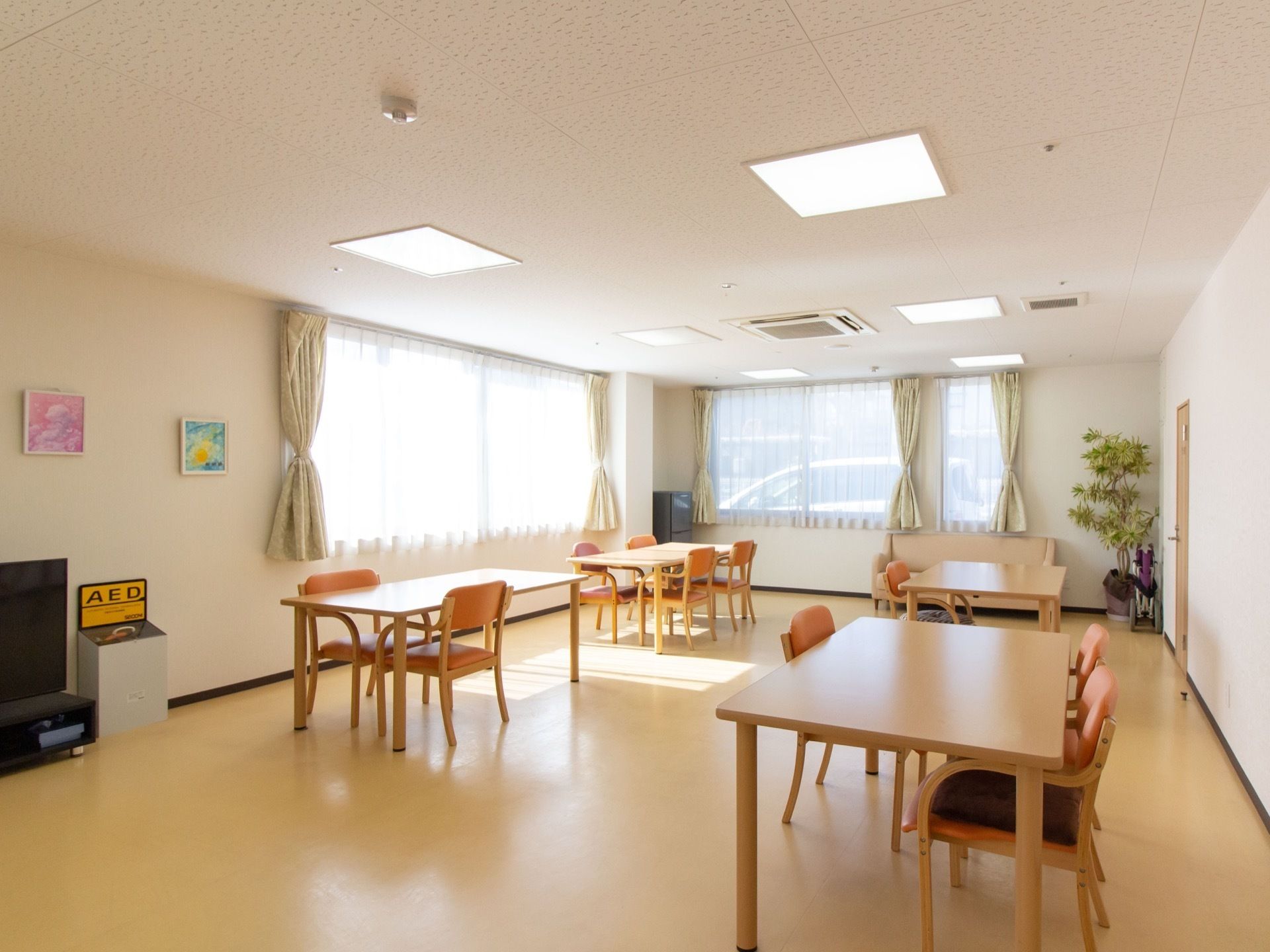 複数のダイニングテーブルと椅子がセッティングされている。フロアの角には観葉植物や冷蔵庫が置かれている。
