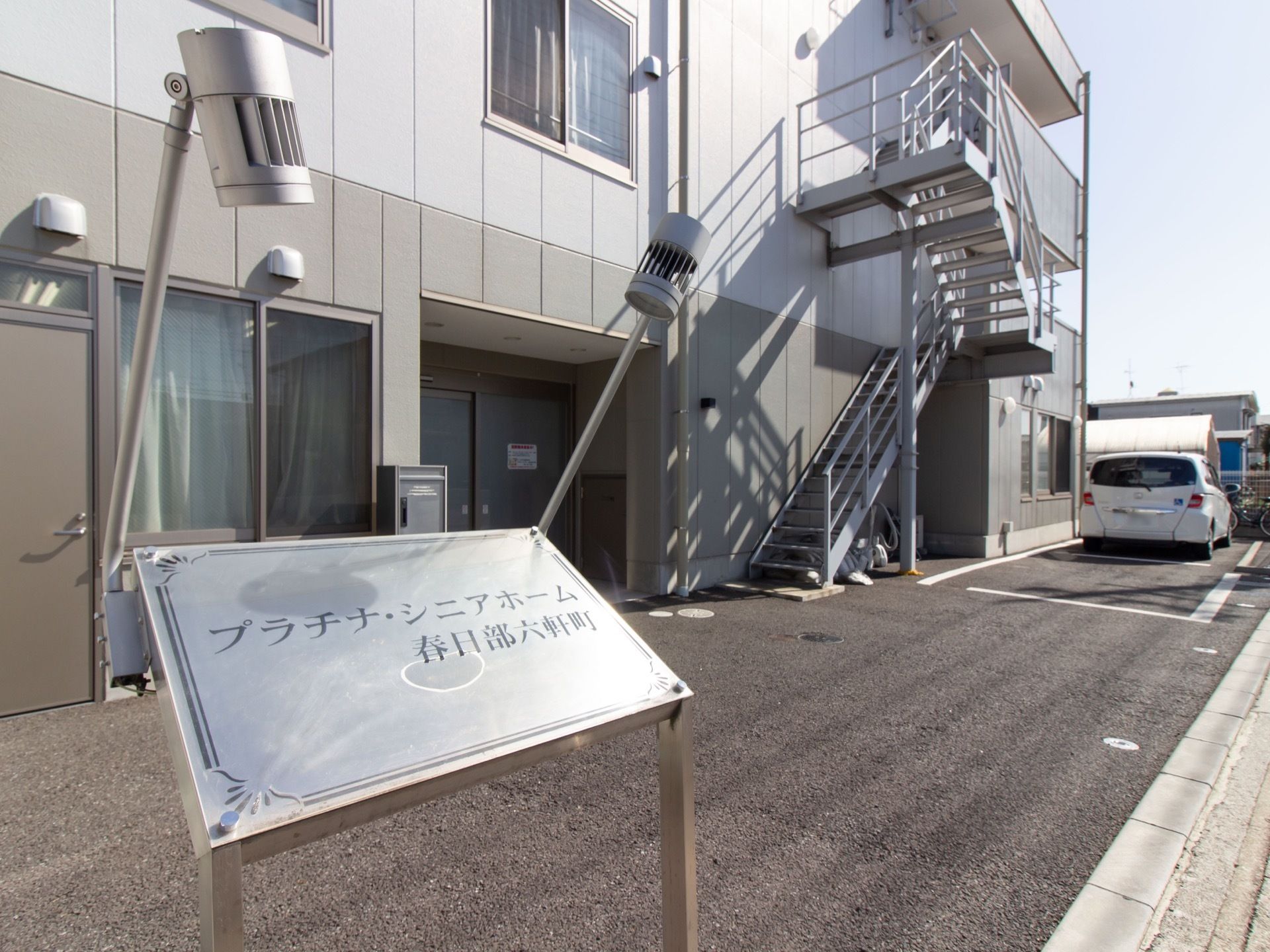 手すり付きの非常階段が完備されている建物である。手前には施設名が書かれた、光沢のある看板が設置されている。
