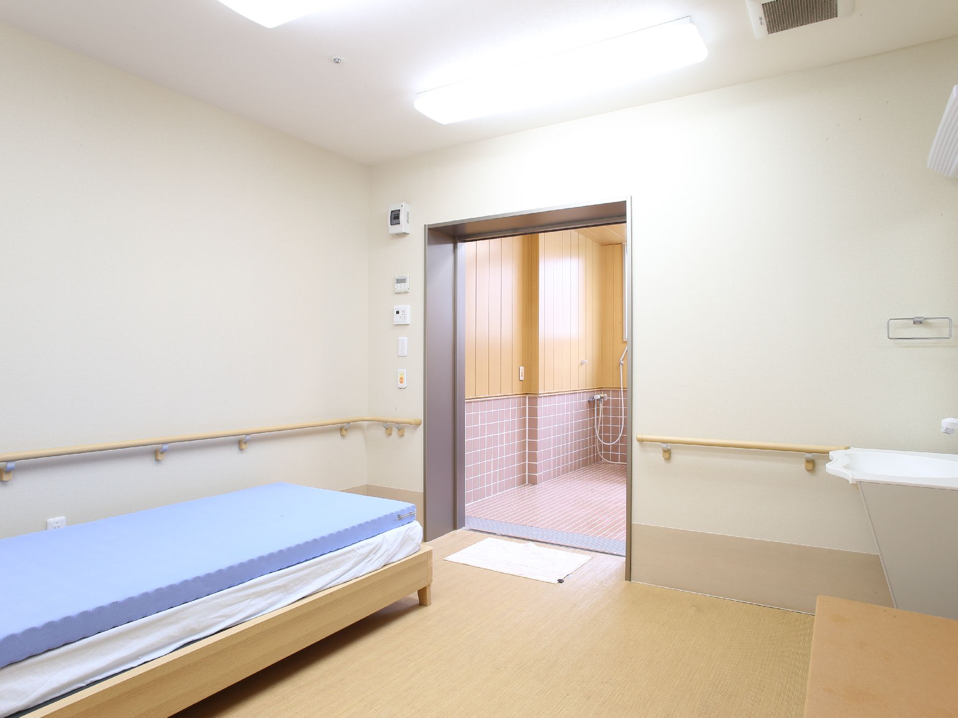 ゆったりとした広さの脱衣所にはベッドが設置されている。壁には手すりとナースコールが付いていて、洗面台が置かれている。