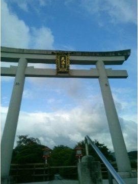 石でできた大きな鳥居。鳥居の前には手すりがついた階段がある。鳥居の奥には緑が見え、自然を感じることができる。