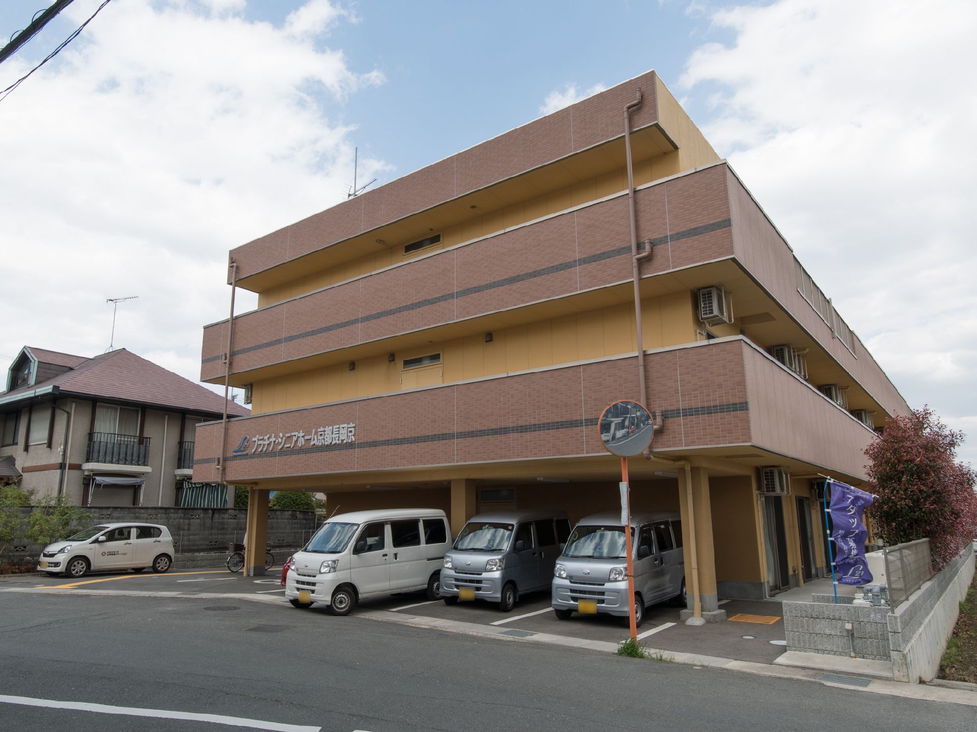 茶色の色調の落ち着いた雰囲気の建物で、施設名が道路から見える外壁に書かれている。駐車場が道路沿いにつくられている。