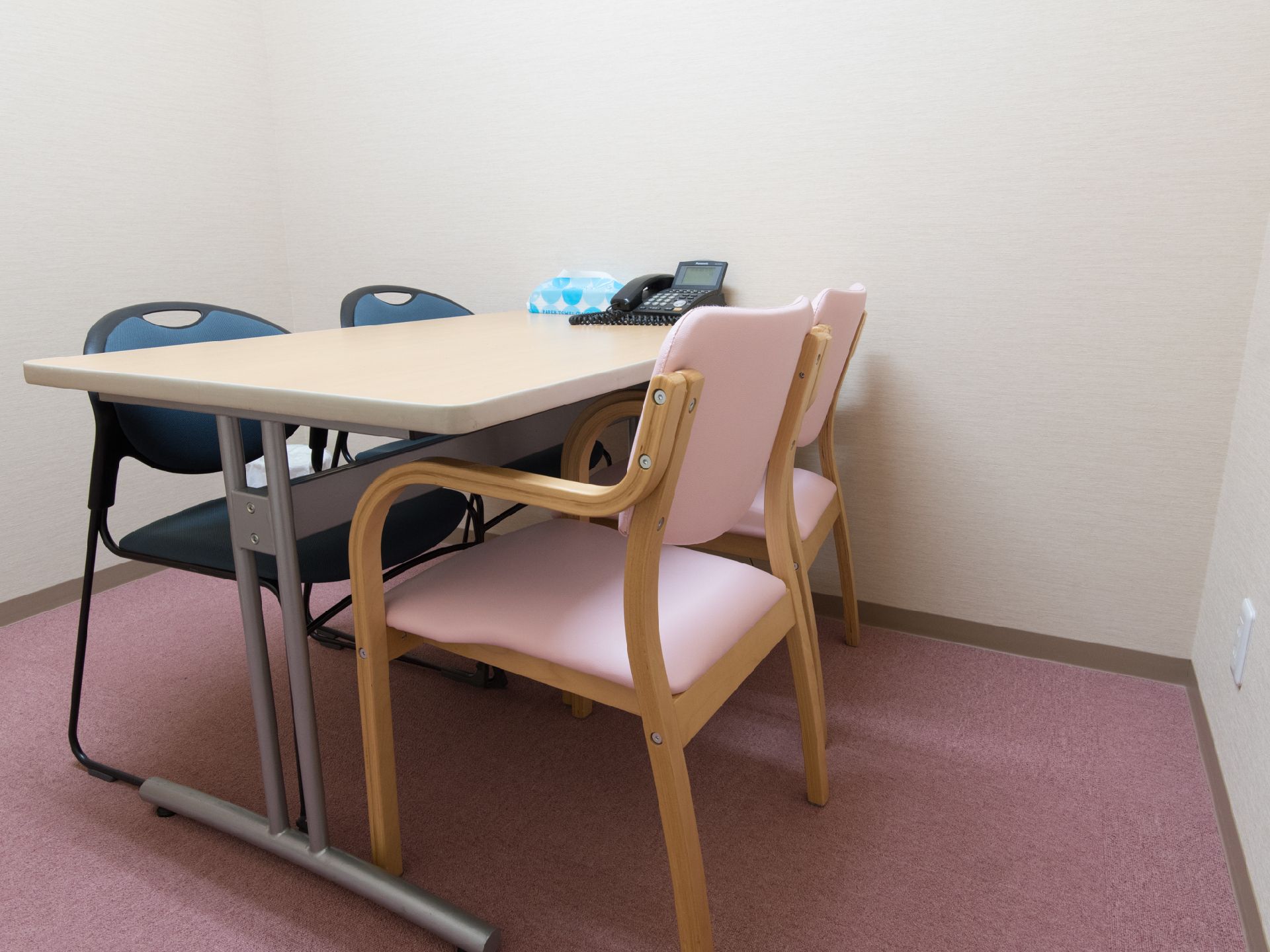 テーブルや椅子がある。電話が置かれている。白の壁で清潔感がある。落ち着いて会話ができる空間となっている。