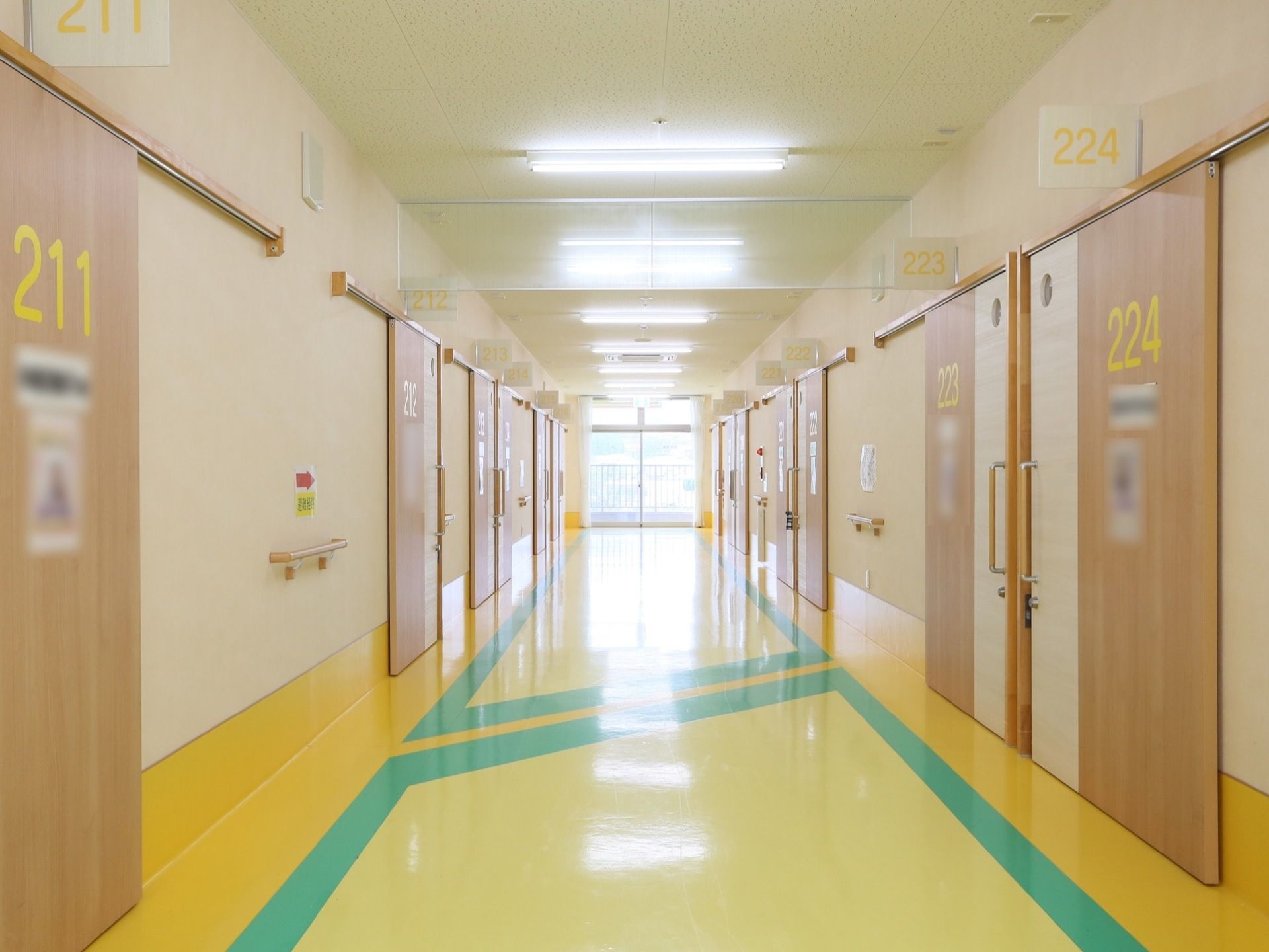 各居室の扉が並んでいる幅の広い廊下である。扉には大きな文字で部屋番号と入居者様の写真が貼られている。