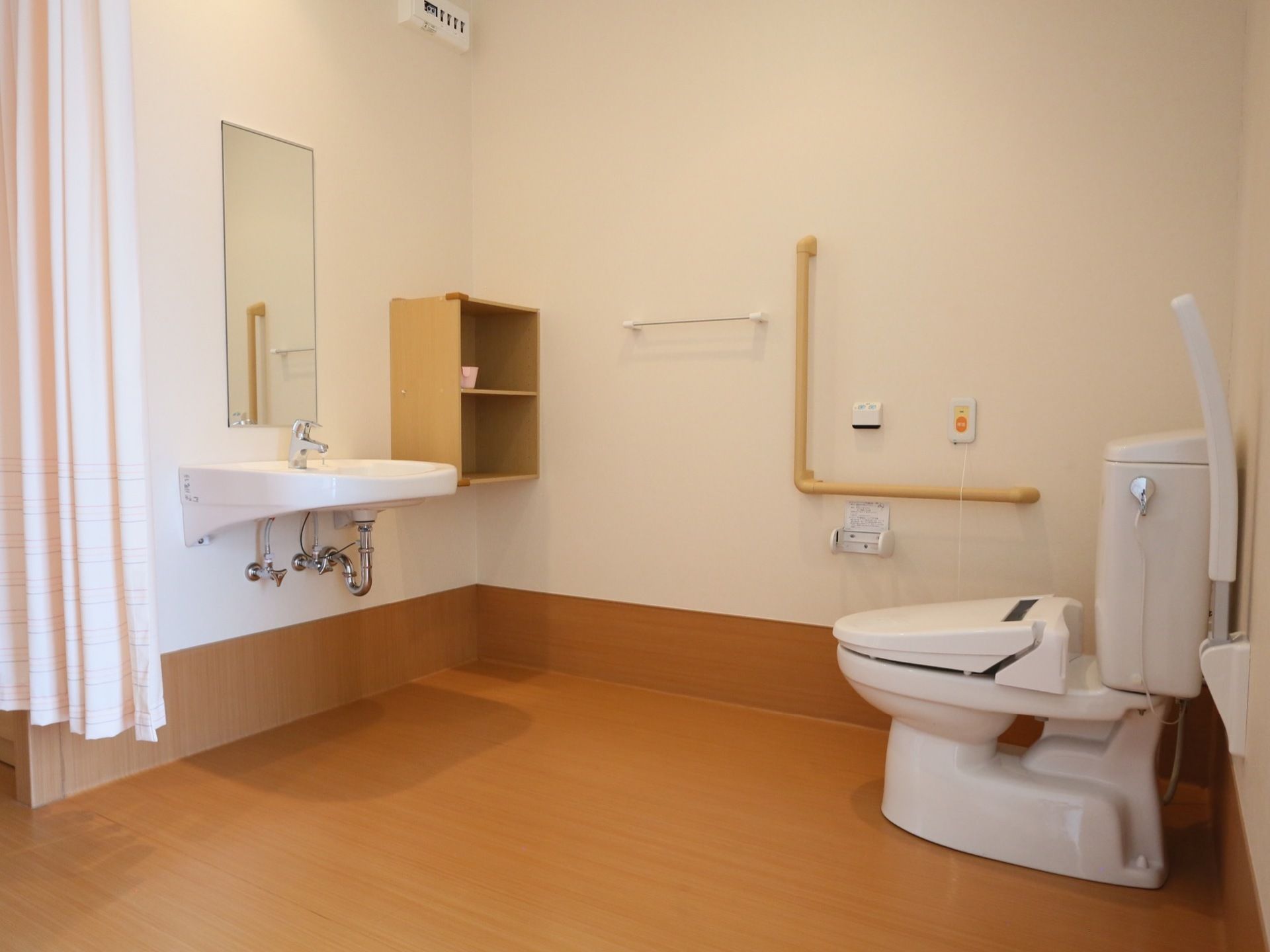 広いトイレである。便器の隣には可動式の手すりが備わっている。また、緊急時呼び出しボタンがあり、万が一の時にも安心である。