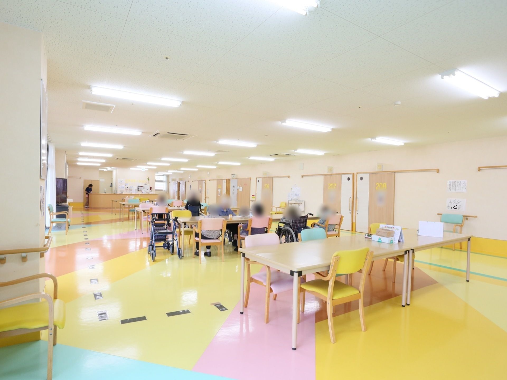 ピンク、黄色、水色で幾何学模様にカラーリングされた床に、同系色の椅子を備えたテーブルが並ぶ食堂