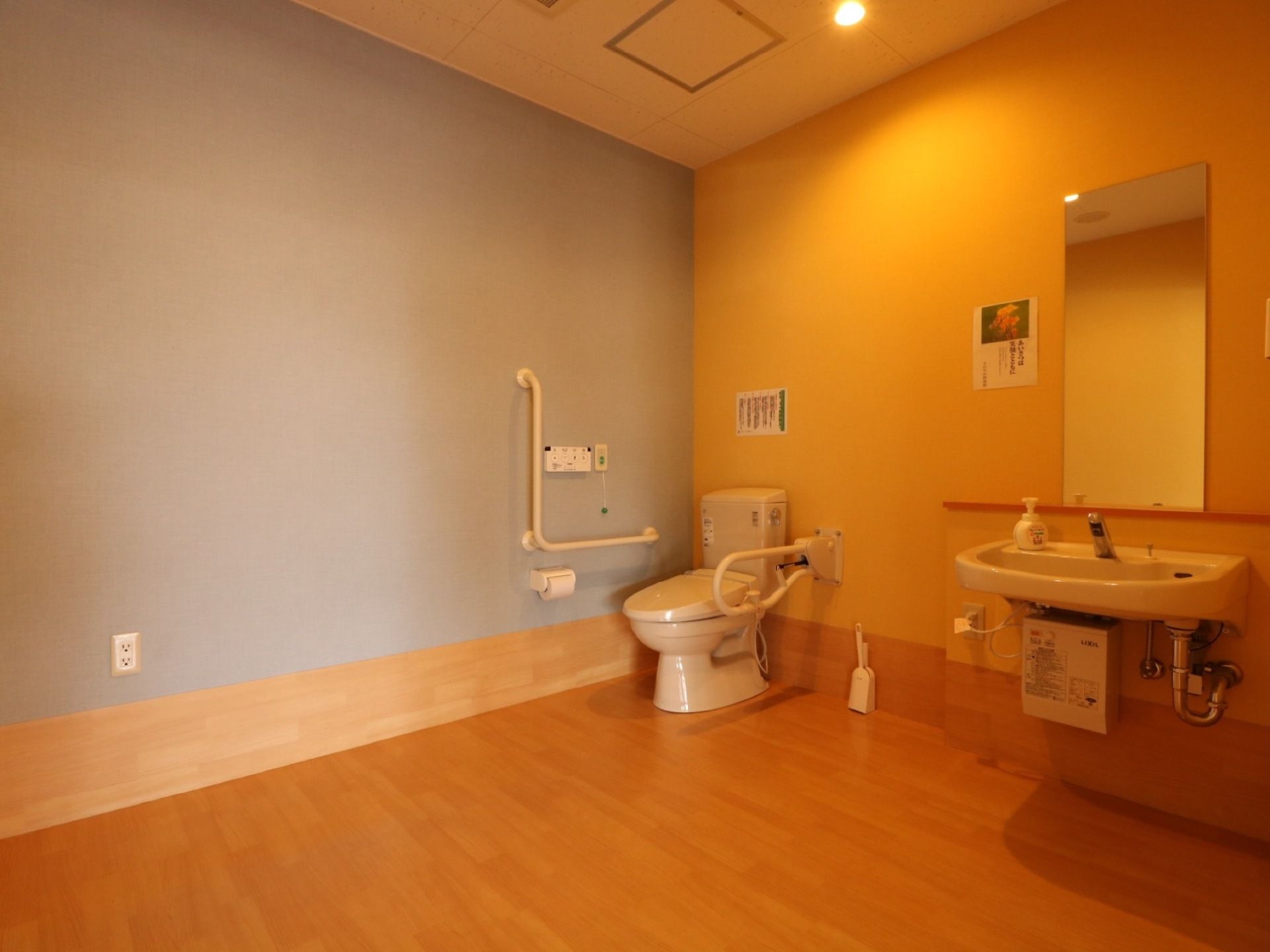 フローリングの広々とした部屋の角に洋式トイレが設置されている。その隣には洗面台があり、壁に鏡が取り付けられている。