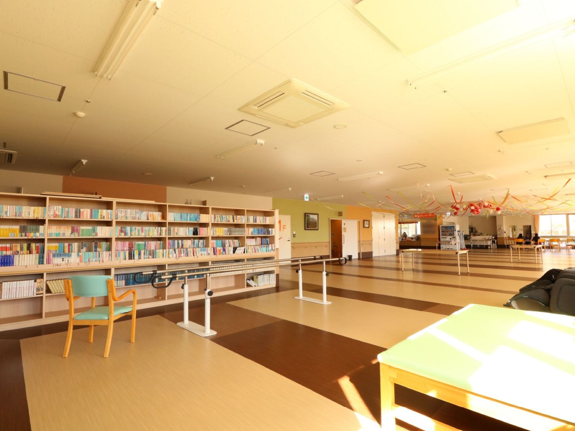 広々とした部屋の壁に大きな本棚が設置され、たくさんの本が収納されている。机や椅子などが置いてあり、奥に自動販売機もある。