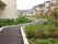 建物の隣に設けられた遊歩道。緩やかなカーブもあり距離が長い。両脇には植物が植えられている。周辺には民家がある。