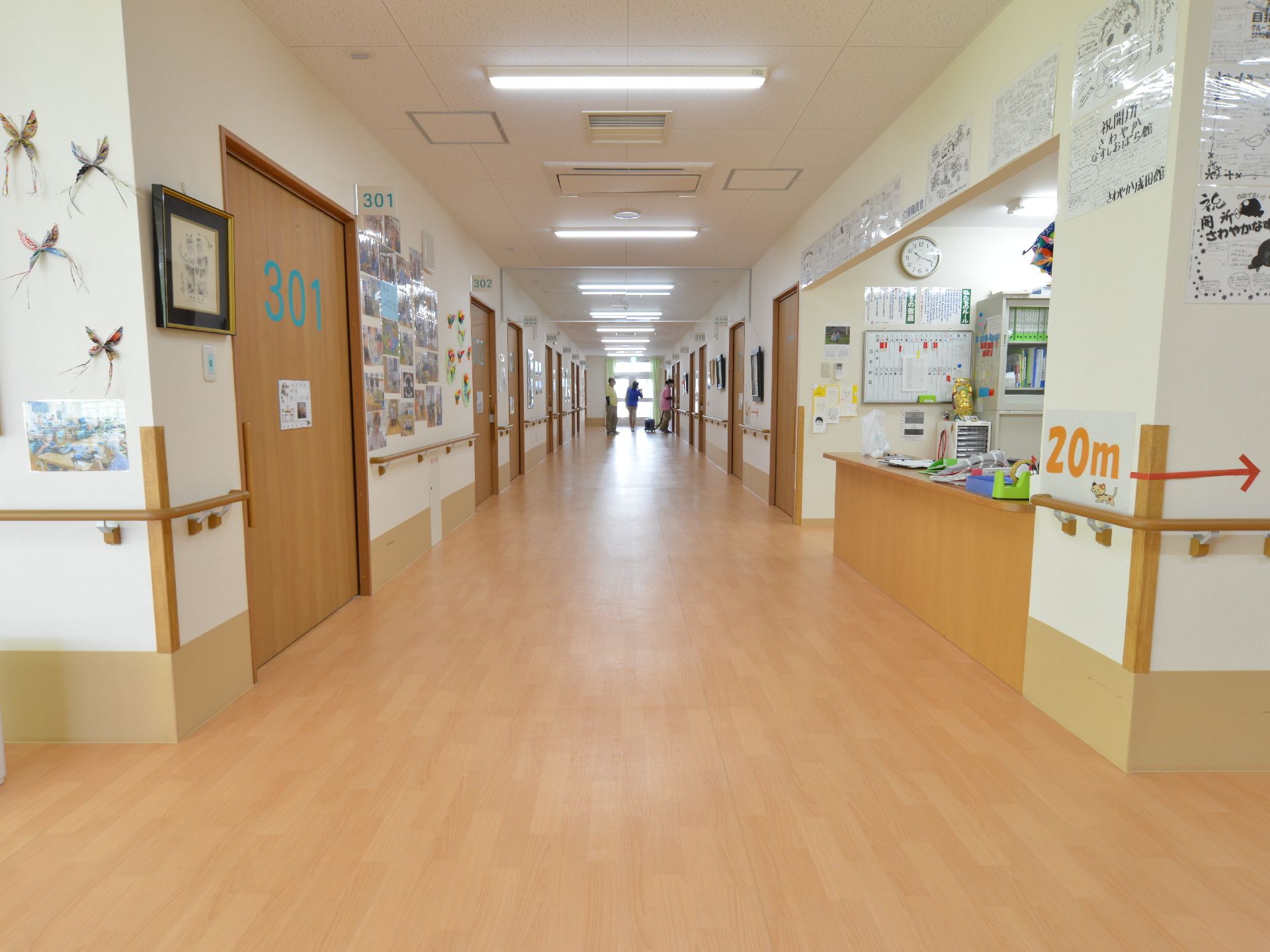 車椅子同士でも楽にすれ違う事が出来る広い廊下。壁には手摺が設置されている。壁には写真や飾り、お知らせ等が貼られている。