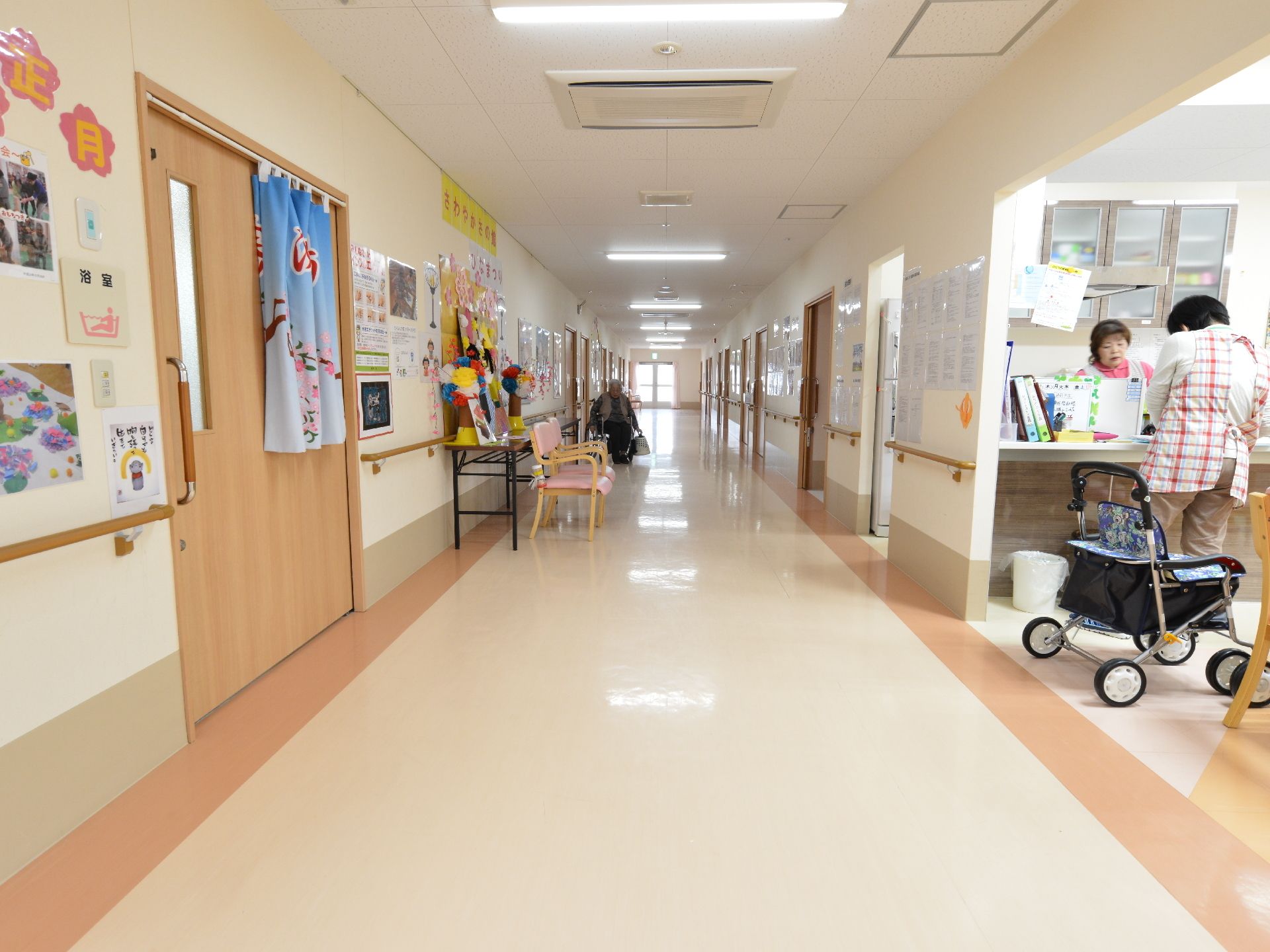 明るいベージュが基調の内装、奥に窓が見え、両側にドアが並んでいる廊下
