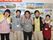 施設スタッフがにこやかにピースサインをして写真に写っている。私服を着用しており首からネームカードを下げている。
