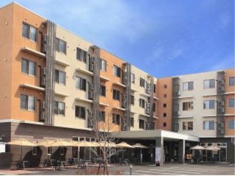 ４階建ての建物前に舗装された駐車スペースがある。建物に沿ってパラソルが置かれ、座って寛げる。玄関にはひさしが付いている。
