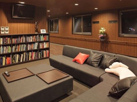片側に窓が並ぶ通路の一角にある共有スペース。コーナー部分が丸みをおびた大きなソファが置かれ、その前には本が沢山入った棚がある。