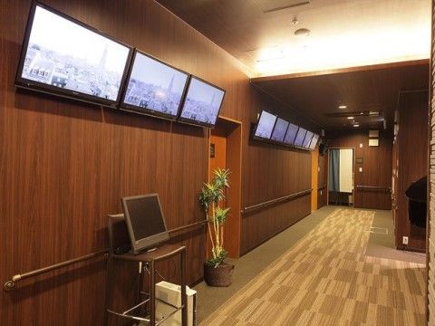 ベージュの絨毯が敷かれた、ゆったりした通路。壁の上部には複数のテレビモニターが並ぶ。全体が落ち着いた雰囲気。