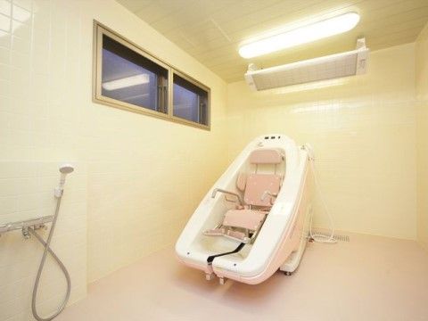 座ったまま入浴できる特殊介助浴槽が置かれている。浴室内は淡いピンクと白のタイル張りで、窓もあり清潔で明るい。