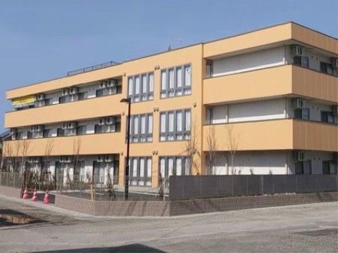 ベージュと白い壁の３階建ての建物である。それぞれの部屋にエアコンの室外機があり邪魔にならないよう窓の上に設置されている。