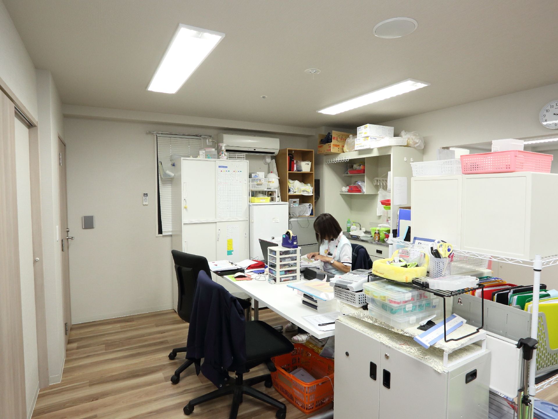 4人が使用できるテーブルが事務室には置かれている。書類の保管棚が複数置かれている。整頓がなされている。