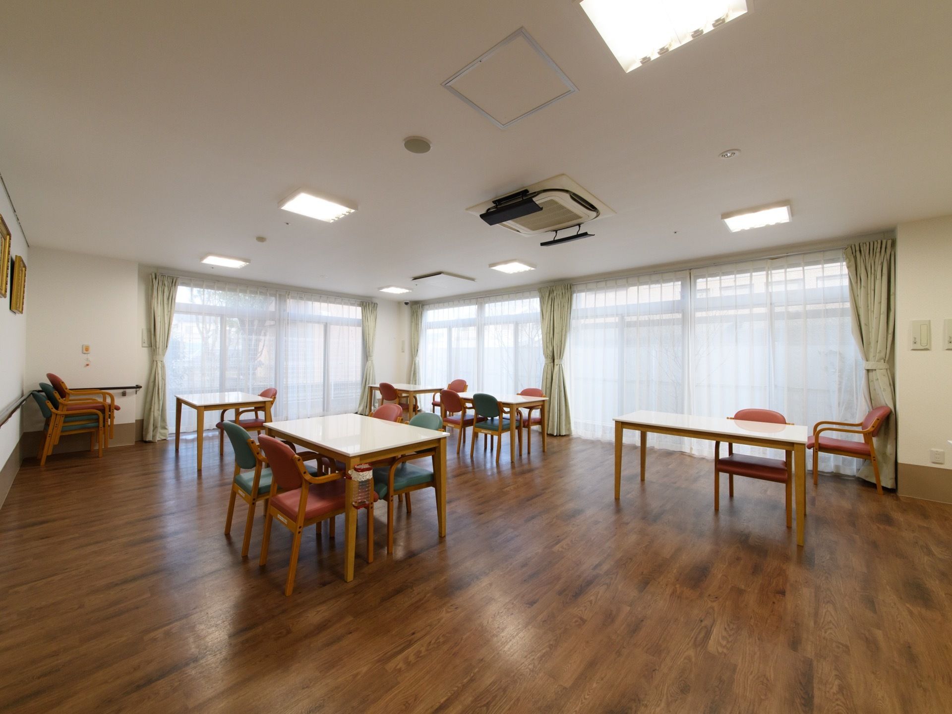 肘掛け椅子とテーブルの設置がいくつかある。部屋の壁の2辺ほどを窓が占めている。窓には薄手のカーテンと厚手のカーテンが取り付けられている。