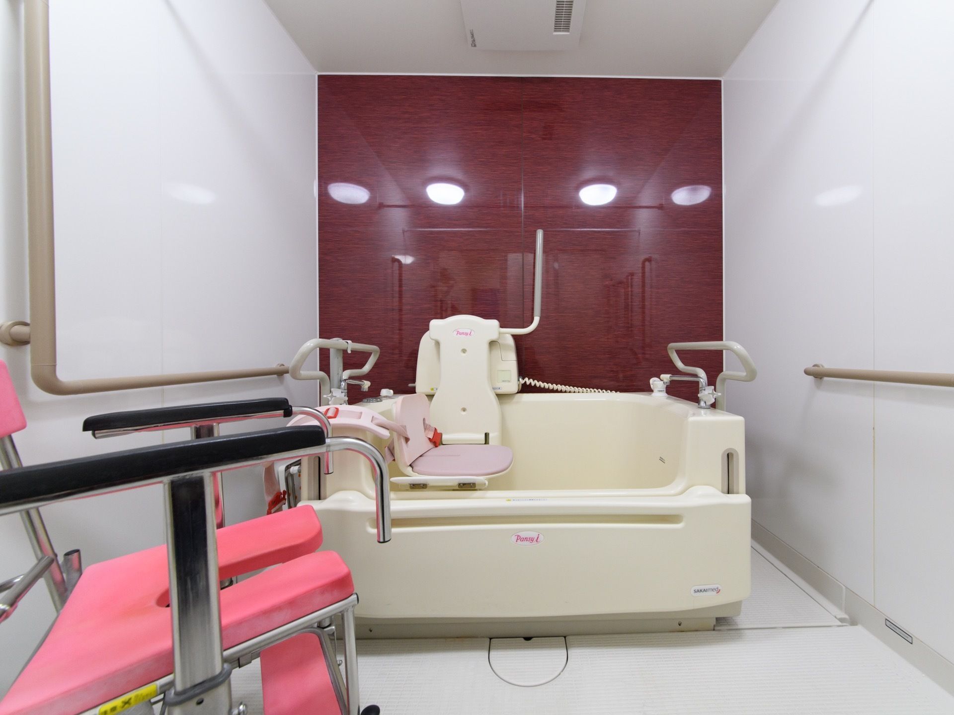 左右の壁、天井、床が白であり、奥の壁が赤色の部屋である。左右の壁には手すりがあり、部屋奥には介護用浴槽が置いてある。