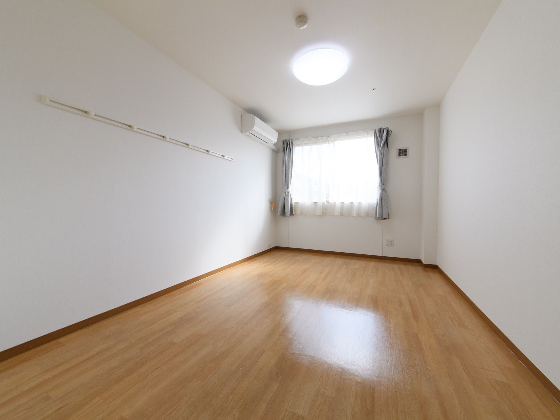 居室は白を基調としていて清潔感のある洋室である。窓も大きく、太陽を取り込むには十分。カーテンも付いているので、光の調節もできる。