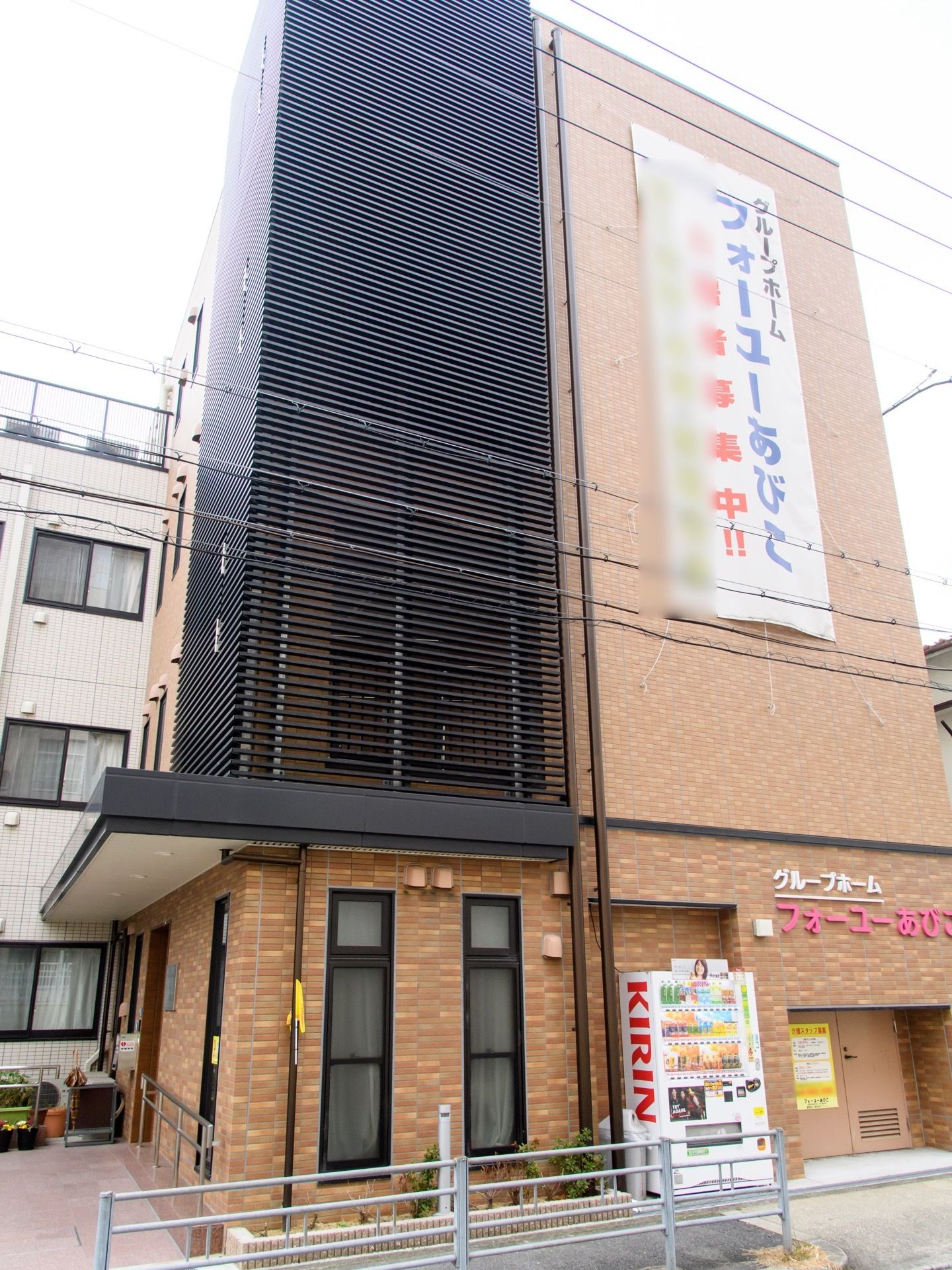 レンガ調の建物である。利用者募集の横断幕が壁についている。ガードレールのついた道路に面しており、自動販売機が備わっている。