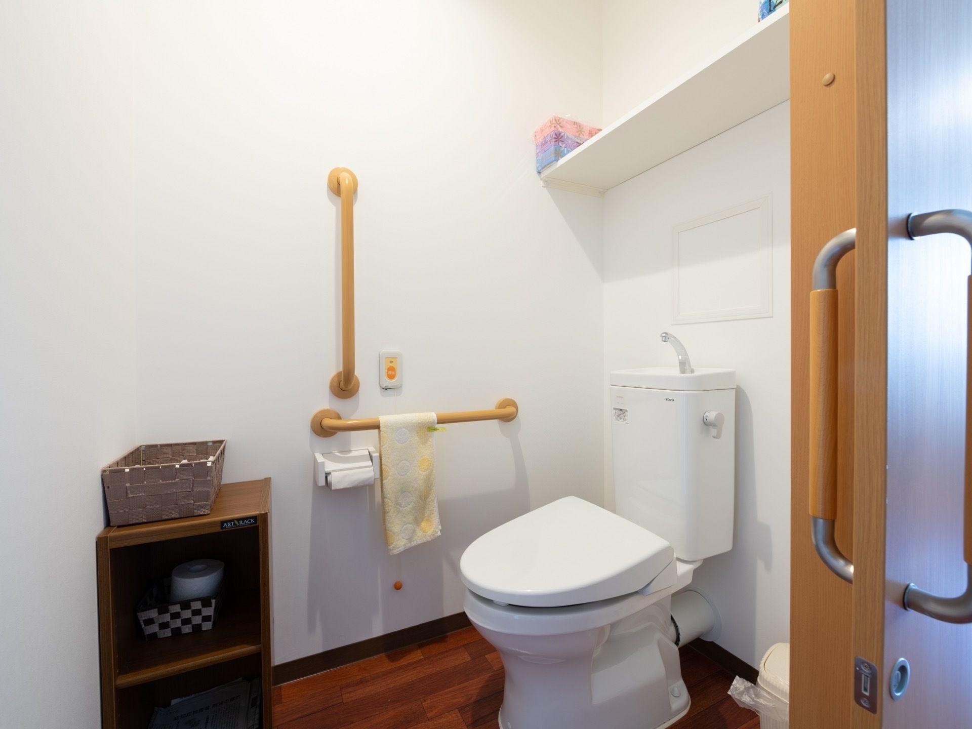 トイレの個室内は広さに余裕がある。頭上や足元に収納棚があり、便座のそばには手すりが取りつけられている。