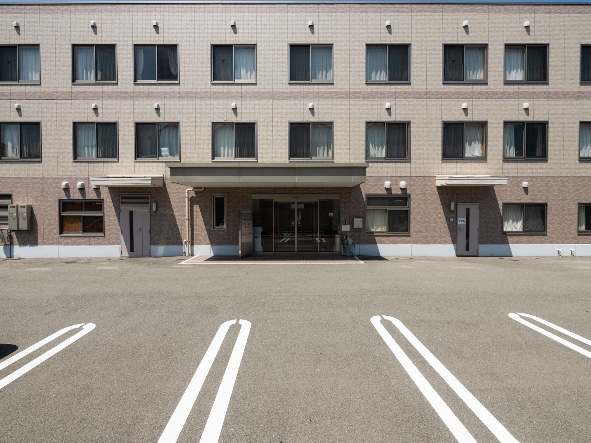 集合住宅のような外観の建物があり、すぐ前の前に駐車スペースがある。入口は軒下があり、雨天時でも濡れずに車の昇降ができる。