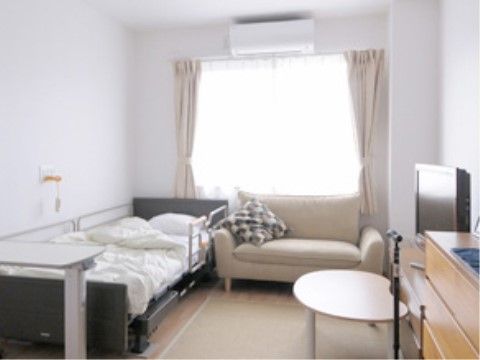 白を基調とした清潔感のある部屋である。ベッド、ソファ、テーブルを配置してもゆとりあるスペースになっている。エアコンが設置されている。