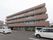 建物に併設された駐車場から撮られた、施設の写真である。駐車場と施設の間には植え込みが設けられ、多数の植物が植えられている。