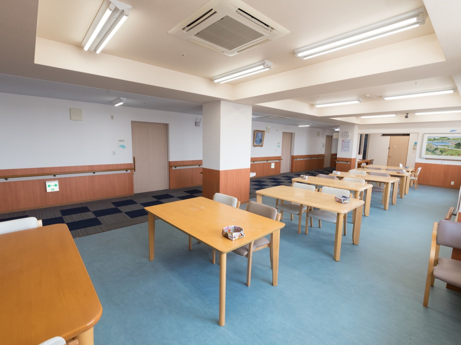 通路と部屋が一続きになっていて、各居室の扉が見える。柱には時計とカレンダーが掛けられ、通路には手すりが設置されている。