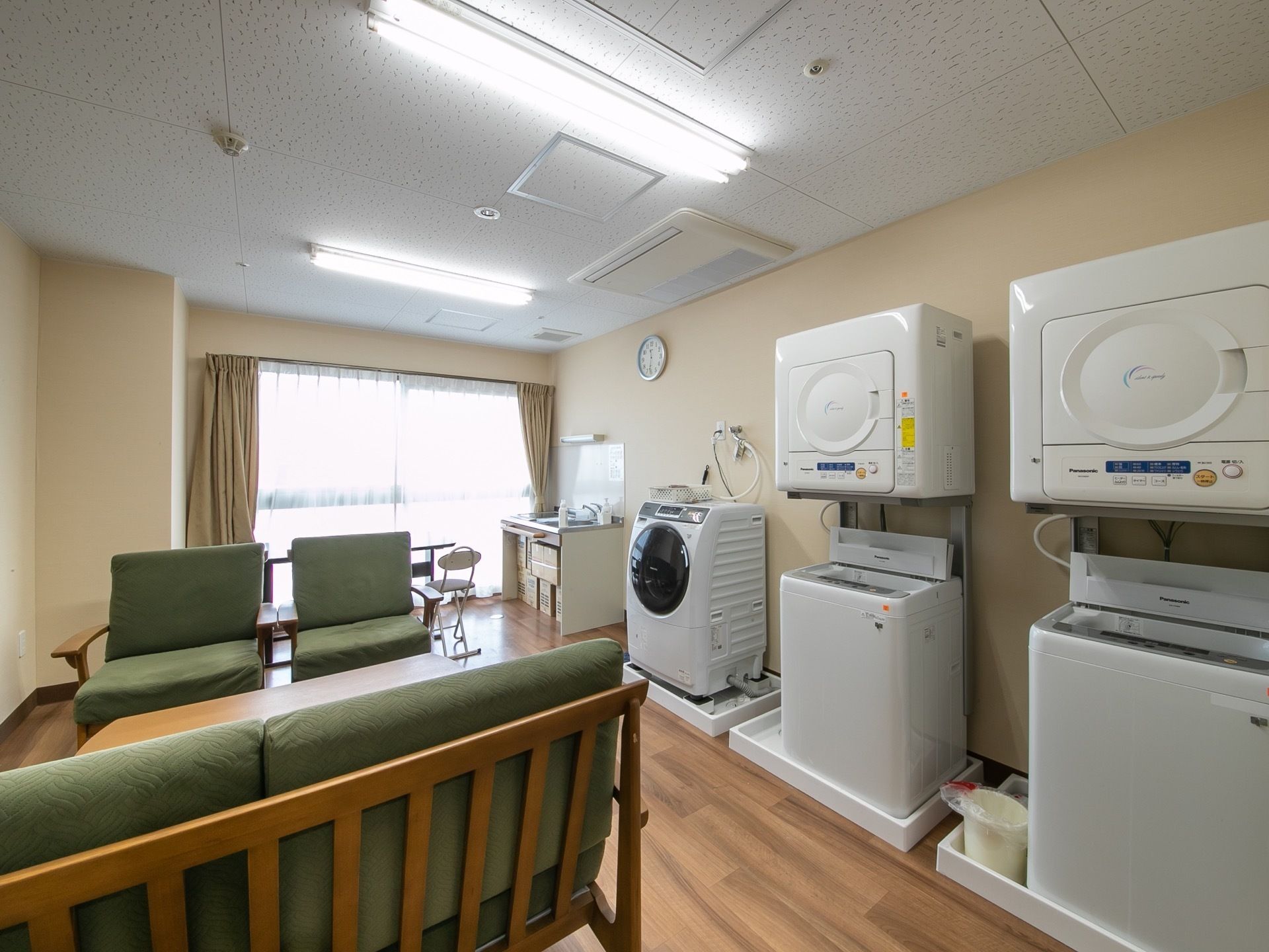 木製のテーブルと椅子が置かれている。横には洗濯機3台と乾燥機2台が設置されている。窓際にはキッチンスペースもある。