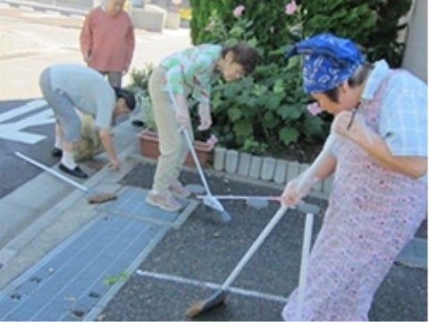 道路際の溝やグレーの通路部分をほうきで掃除している4人の人物