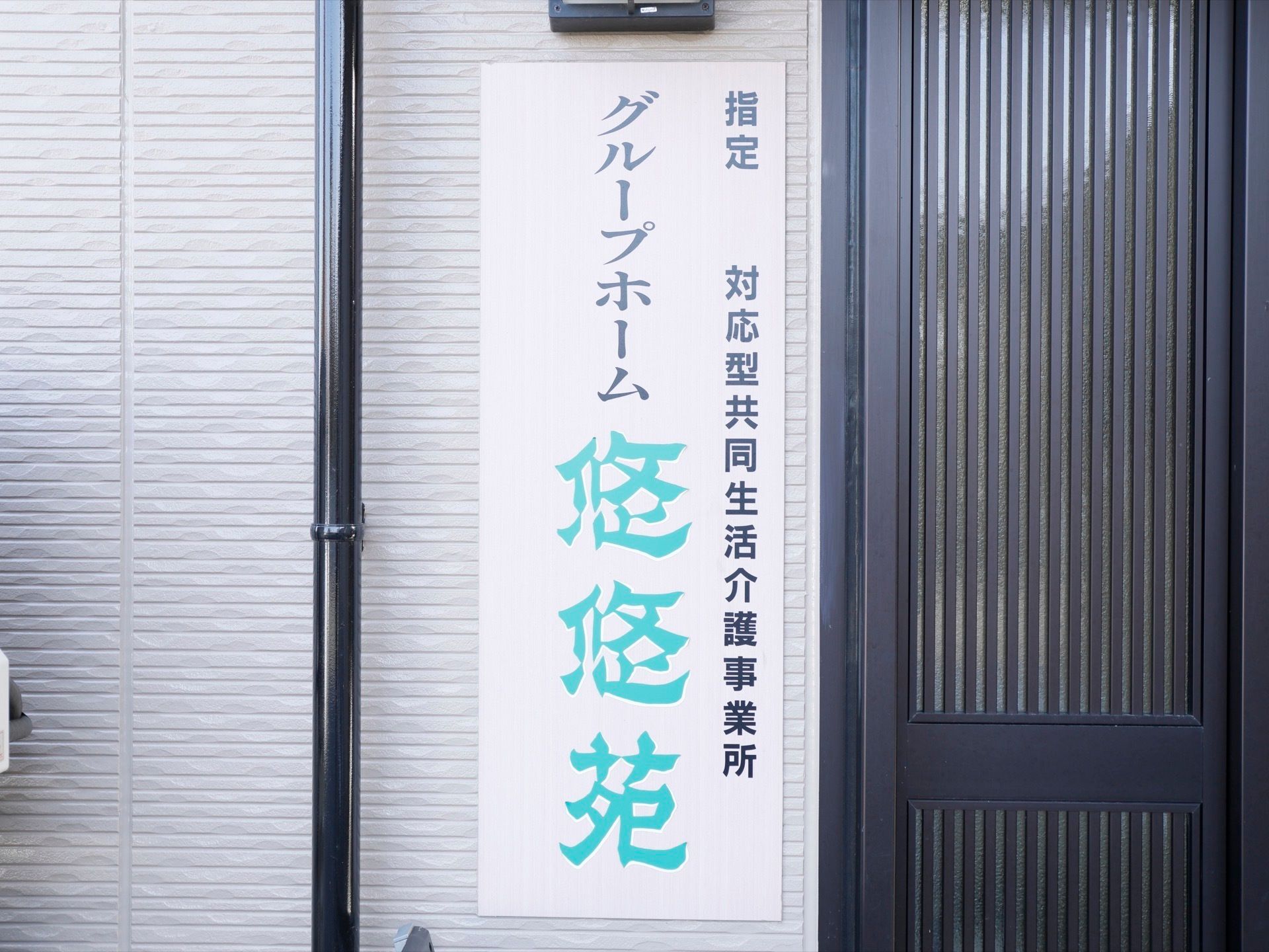 施設の玄関には左側の壁に大きく施設名を表示している。白い地にブルーグリーンの文字で、遠くからでも目につきやすい。