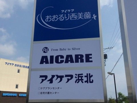 青い看板に施設名が表記されている。看板の後ろにはアイボリーとブラウンのモダンな施設の建物があり、落ち着いた雰囲気である。