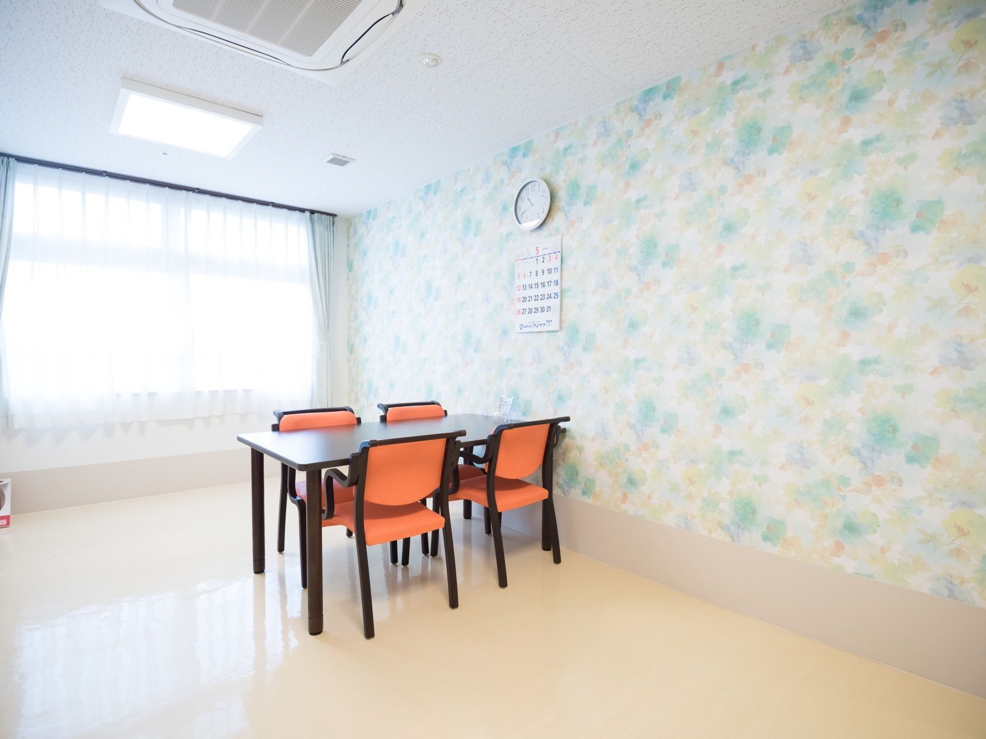 パステルカラーの壁紙が印象的な談話スペースで、壁には時計やカレンダーが掛けられている。大きな窓からは外光がたっぷりと差し込む。