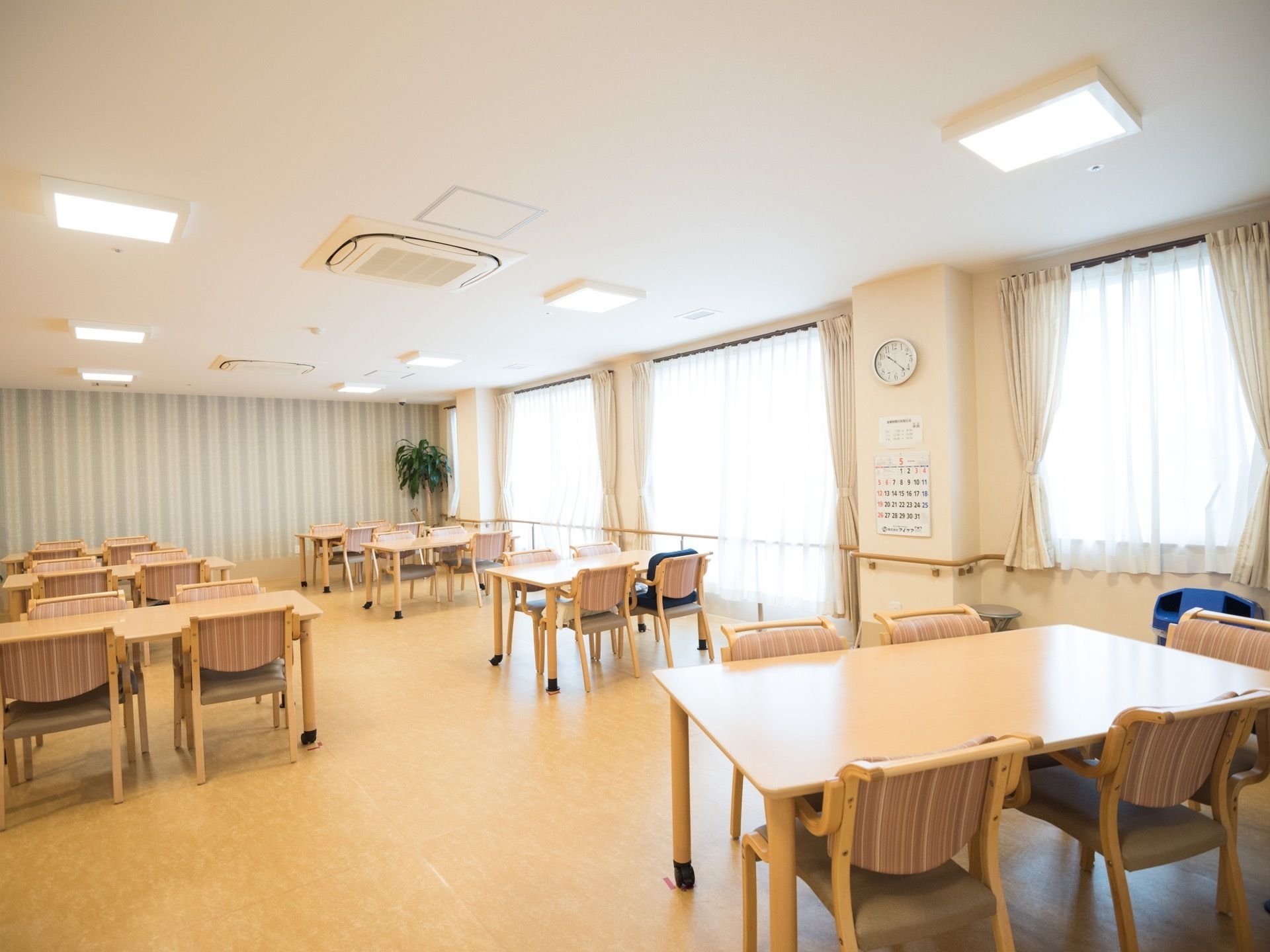 空調設備が整っている明るい食堂で、天井には複数の照明が設置されている。壁には手すりが取り付けられている。