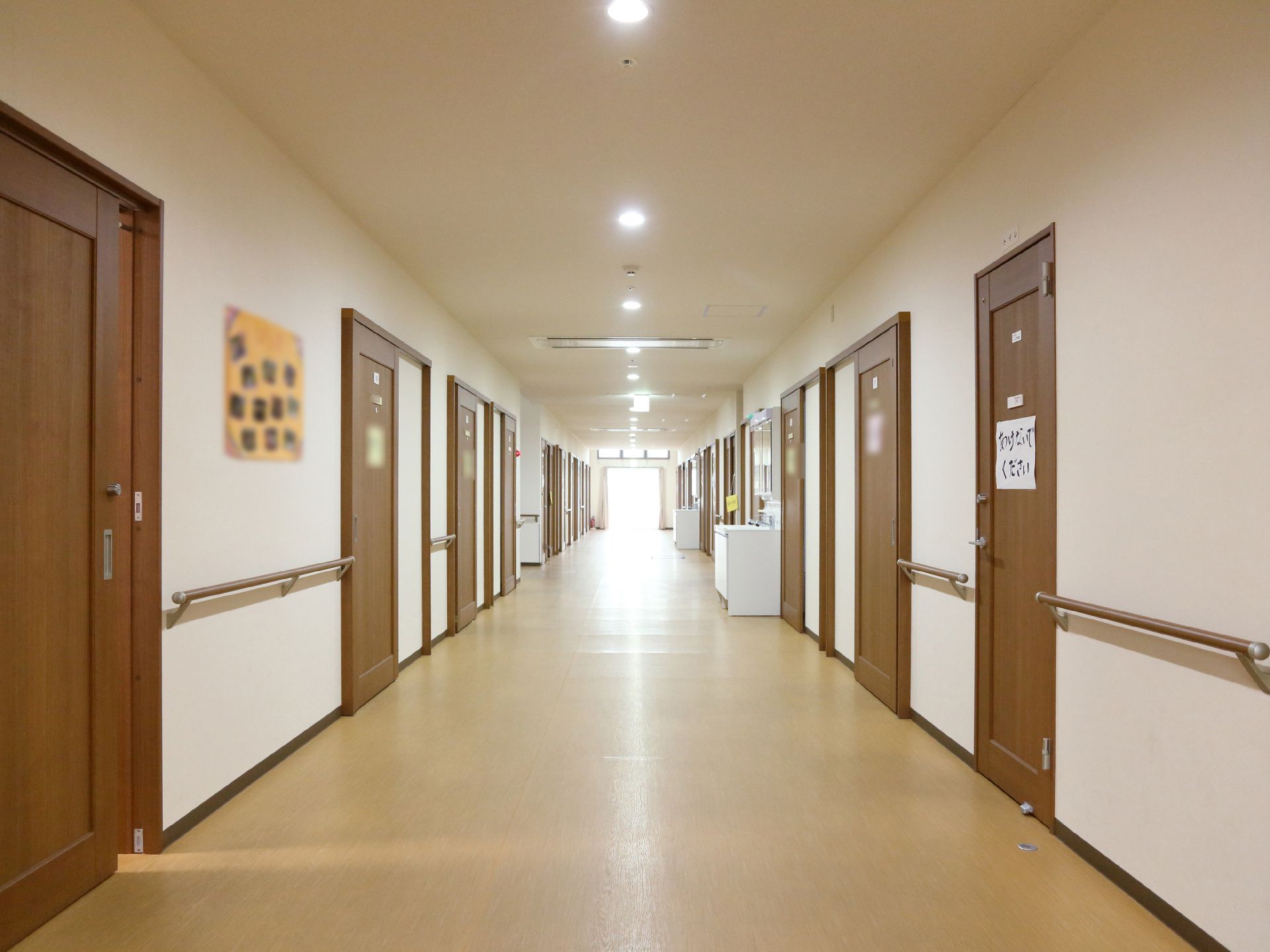 廊下の壁には壁には手すりが設置されている。天井には小さい丸いライトが並んでいる。居室の扉は濃いブラウンで重厚感がある。