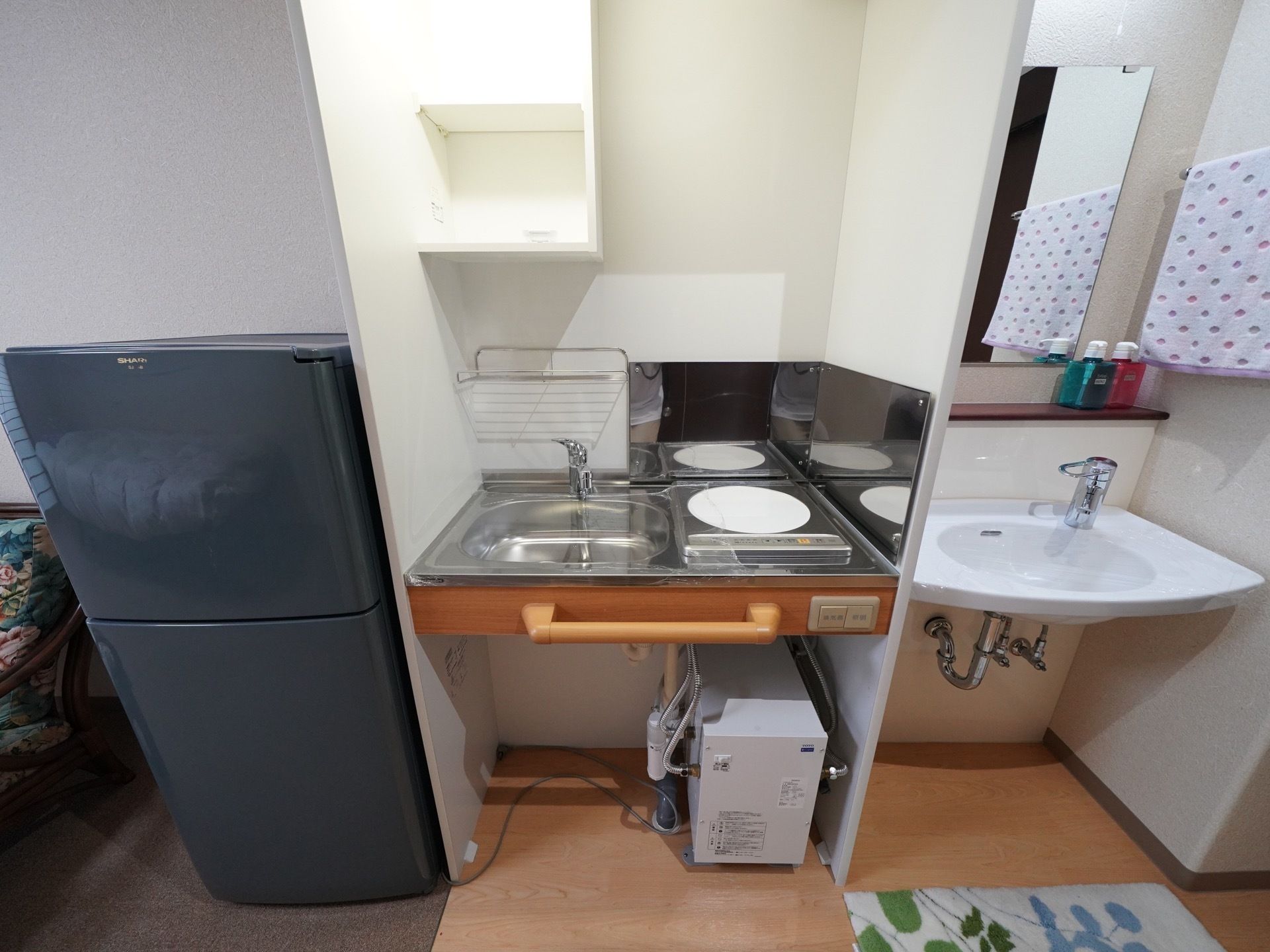 居室に、流し台と、掃除が簡単にできるIHコンロを備えたミニキッチンがある。その隣には冷蔵庫が設置されている。