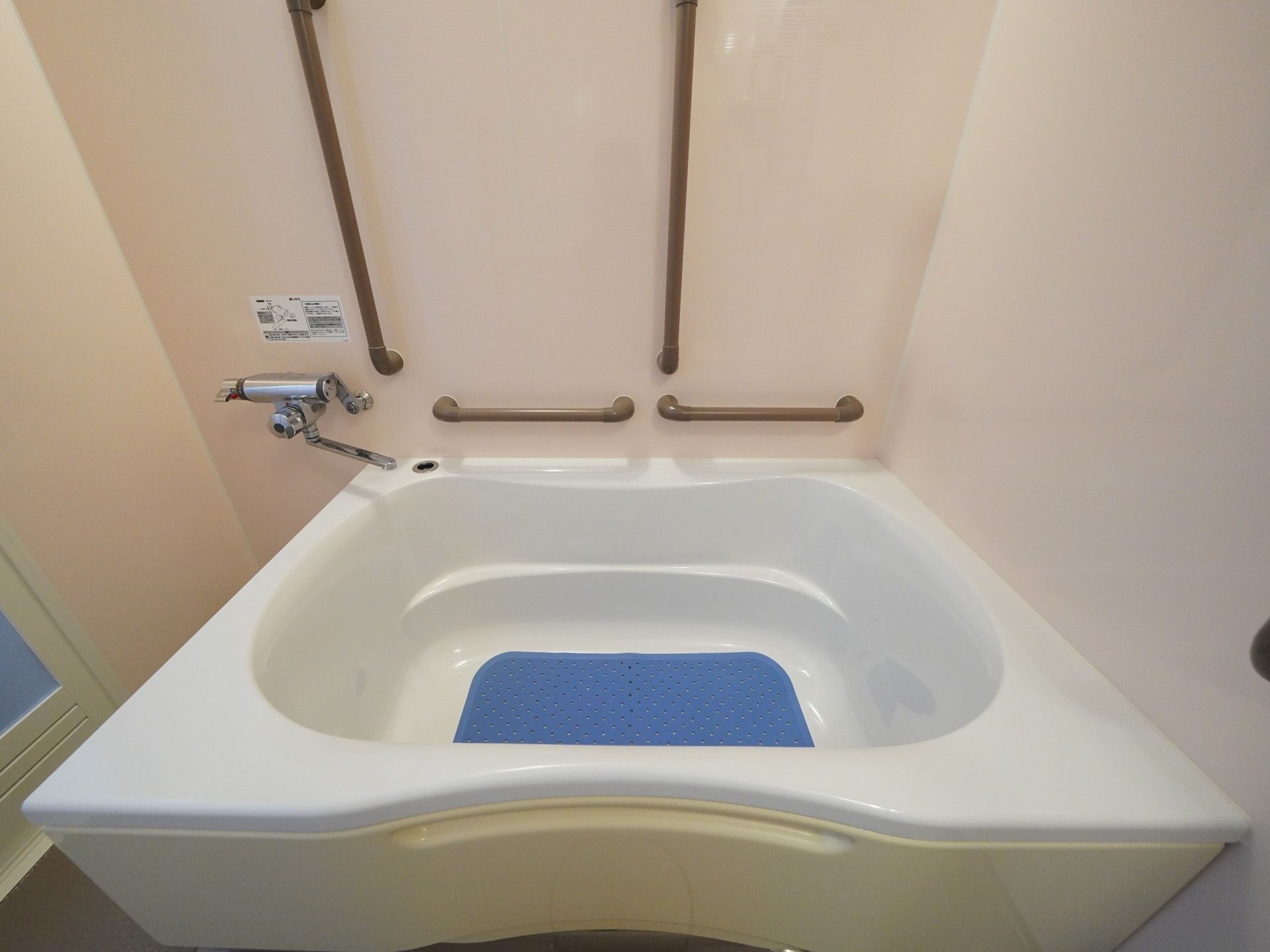 ベージュ色の壁にブラウンの手すりが設置された、掃除が行き届いた浴室である。浴槽があり、ゆっくりお湯に浸かってくつろぐことができる。